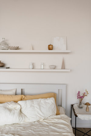 Minimalistic interior of bedroom with white bed and wooden shelves above it with decorの写真素材