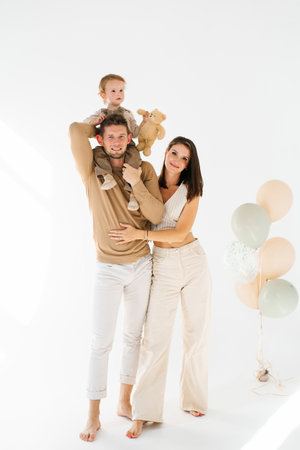 Young mother and father are holding son and teddy bear against a backdrop of balloonsの写真素材