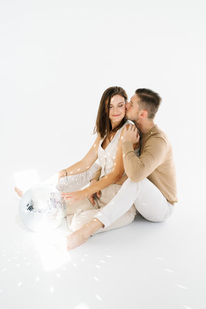 Couple is sitting on the floor, kissing each other with disco ball is in the backgroundの写真素材