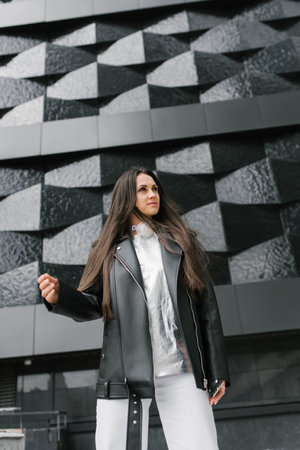 Stylish woman in a black jacket stands in front of a buildingの写真素材