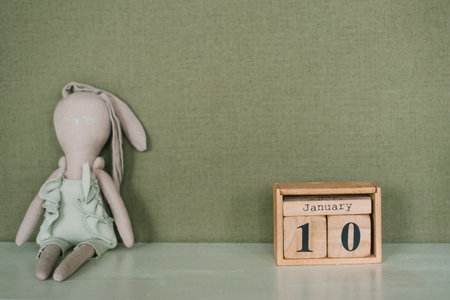 Stuffed rabbit sits on a table next to a wooden calendarの写真素材