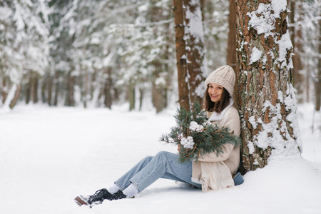 Woman is sitting in snow with hat on and holding bouquet of pine needlesの写真素材