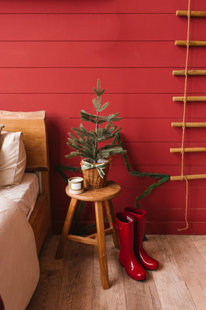Christmas tree is on a stool in front of a red wall in bedroom. Cozy and festiveの写真素材