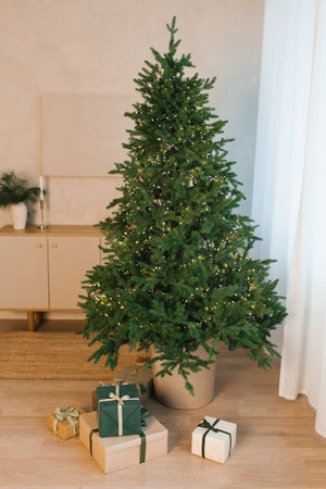 Christmas tree with lights and presents on it is in front of a white curtain in living roomの写真素材