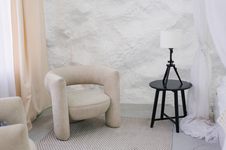 Modern lamp is on a table next to the chair. Room is empty and has a minimalist feelの写真素材