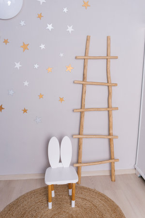 White chair rabbit sits in front of a wooden ladder and children room decorated with starsの写真素材