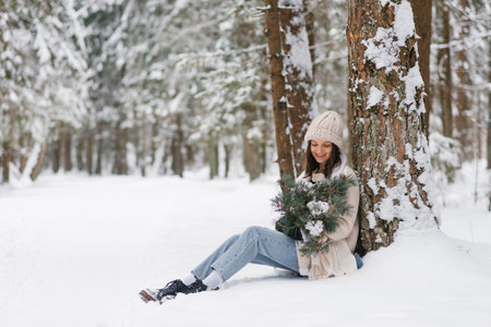 Young woman is sitting in the snow with bouquet of flowers in her lapの写真素材