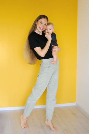 Young happy woman is holding baby in arms at homeの写真素材