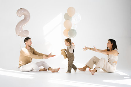 Two year old birthday boy goes from mom to dad against the background of festive balloonsの写真素材
