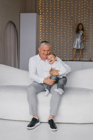 Father is holding son child on couch. Scene is warm and loving, with the man and baby sharing special moment togetherの写真素材