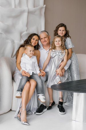 Happy family of five is posing for photo in front of couch. People are wearing silver dresses and suits, and they are all smilingの写真素材