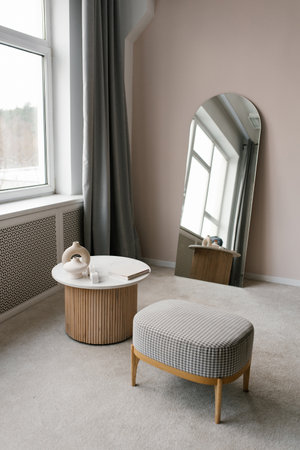 Small room with a white table and a wooden ottoman. Mirror is on the wallの写真素材