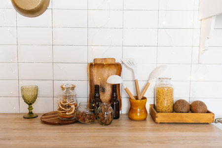 Kitchen counter with variety of items including wooden cutting board, bottle of wine, bottle opener, spoon, knife, bowl, jar, cup, vase and bowlの写真素材