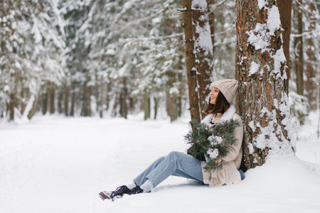 Young woman sits in snow with bouquet of pine branches and cottons in her lap. Scene is peaceful and serene, with the snow covered trees in the backgroundの写真素材