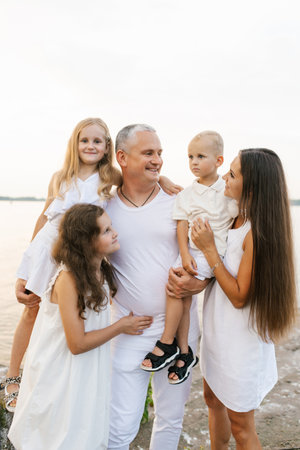Family of five is posing for picture on beach. Man is holding a babyの写真素材