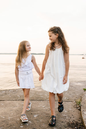Two young girls are walking on beach, holding hands. The scene is peaceful and sereneの写真素材