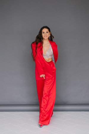 Caucasian young woman in red suit and pants poses for photo. Concept of confidence and sophisticationの写真素材