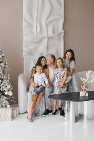 Happy family of five is posing for a picture in front of Christmas tree. Scene is warm and festive, as the people are gathered together to celebrate the holiday seasonの写真素材