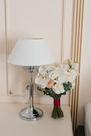 A soft and elegant setting featuring a white flower bouquet next to a table lamp with a neutral background.の写真素材