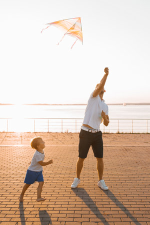 A father holds a vibrant kite as his son watches, enjoying a playful moment outdoors by the waterfront.の写真素材