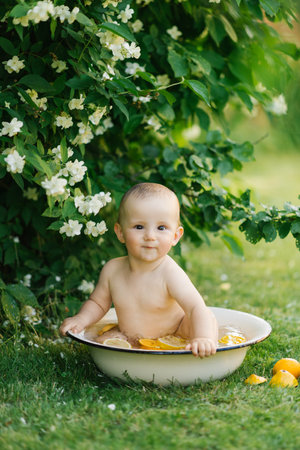 A baby sitting in a white bowl with water and citrus slices, surrounded by greenery and blooming jasmine flowers.の写真素材