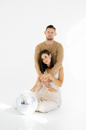 Young man and woman are posing for a picture with a disco ball in the background. Scene is fun and light hearted, as the couple is embracing and enjoying the momentの写真素材