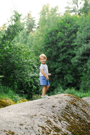 A happy child exploring the beauty of nature while standing on a large rock in a green forest, enjoying the summer outdoors.の写真素材