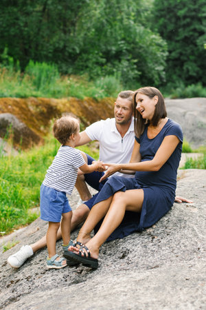 A family of three, including a pregnant mother, father, and young son, sharing a playful and joyful moment together in a summer forest.の写真素材