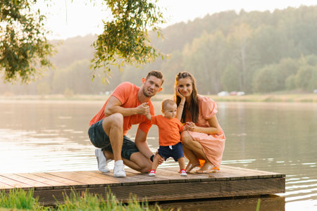 A cheerful family of three enjoying their time together on a wooden dock by the lake under a golden sunset.の写真素材
