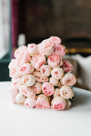 A lush bouquet of pink peonies displayed on a table in a bright and elegant interior, creating a calm and romantic atmosphere.の写真素材