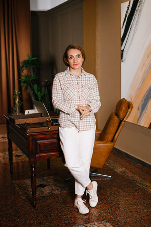 A thoughtful woman standing near a wooden desk in a stylish office setting, with elegant decor and a modern atmosphere.の写真素材