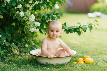 A baby sitting in a bathtub filled with water and orange slices, with a joyful smile, surrounded by greenery and flowers.の写真素材