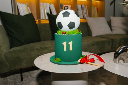 A decorative football cake with a soccer ball design, displayed on a green base, set in a cozy interior environment.の写真素材
