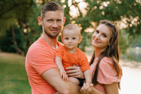 A cheerful family with a young toddler posing outdoors during golden hour. Parents and child dressed...