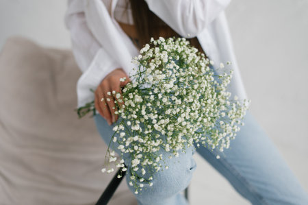 Stylish woman in a white shirt holding a bouquet of white gypsophila, showcasing elegance and natural simplicity in a bright interior.の写真素材