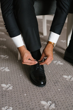 The groom adjusts the laces on polished black leather shoes, wearing a tailored black suit and white shirt.の写真素材