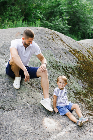 A father sitting on a large rock outdoors, enjoying a peaceful moment in a natural green environment.の写真素材