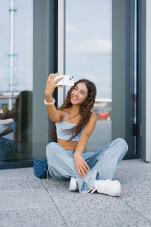 Teen girl sitting on the ground and taking a selfie with her smartphone. Representing the confident and playful essence of Generation Alpha.の写真素材