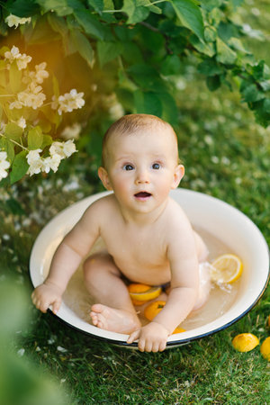 A baby sitting in a white bowl with water and citrus slices, surrounded by blooming jasmine flowers and greenery.の写真素材
