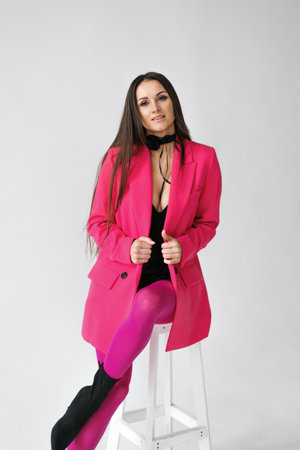 A fashionable woman posing confidently in a bright pink suit against a minimalist white background. The concept illustrates bold fashion and modern femininity.の写真素材