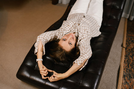 A playful woman lying upside down in a black leather chair in a cozy psychotherapist's office, enjoying a moment of relaxation.の写真素材