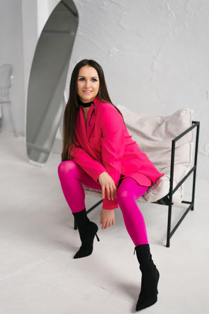 Stylish woman in a bright pink outfit sitting confidently, representing individuality and self-expression in a minimal white studio.の写真素材