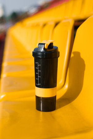 Black and yellow shaker placed on a bright yellow stadium seat, captured in a minimalistic and vibrant composition.の写真素材