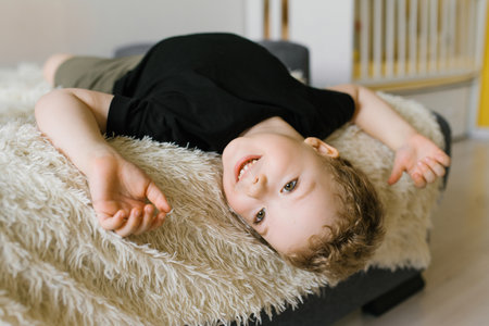 A cheerful young boy lying on a soft white blanket, looking relaxed and happy in natural light.の写真素材