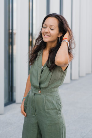 A smiling millennial woman in a green jumpsuit enjoying the day, showing confidence and timeless...