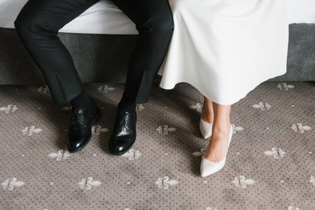 Close up of the bride's elegant white shoes and groom's black leather shoes, capturing wedding attire details on a patterned carpet.の写真素材