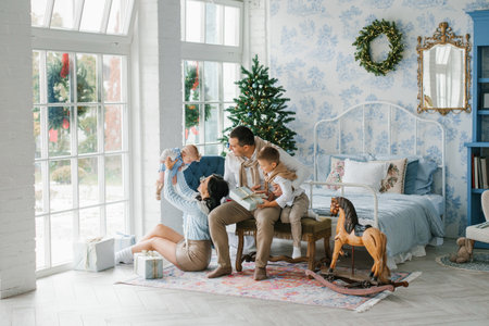 Smiling parents playing with their children near a decorated Christmas tree in a cozy festive home. Perfect for holiday advertising, family lifestyle campaigns, and seasonal marketing visuals.の写真素材