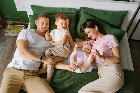 Relaxed parents with two children spending time together in a bright living room, ideal for lifestyle, family life, and parenting concepts.の写真素材