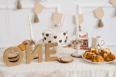 First birthday table with white cake decorated with chocolate bear shapes, wooden letters, pastries...