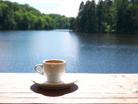 Coffee cup resting on a wooden railing with a lake in the backgroundの写真素材